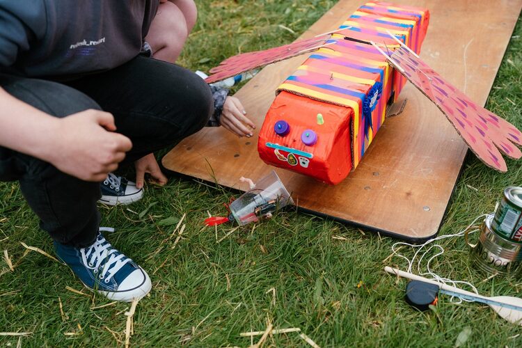 Colourful, simple toy robots pushing each other off a board at EMF Hebocon